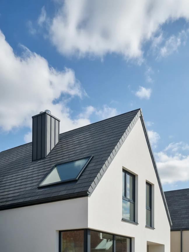 Dark shingle roof with a skylight and chimney under a blue sky